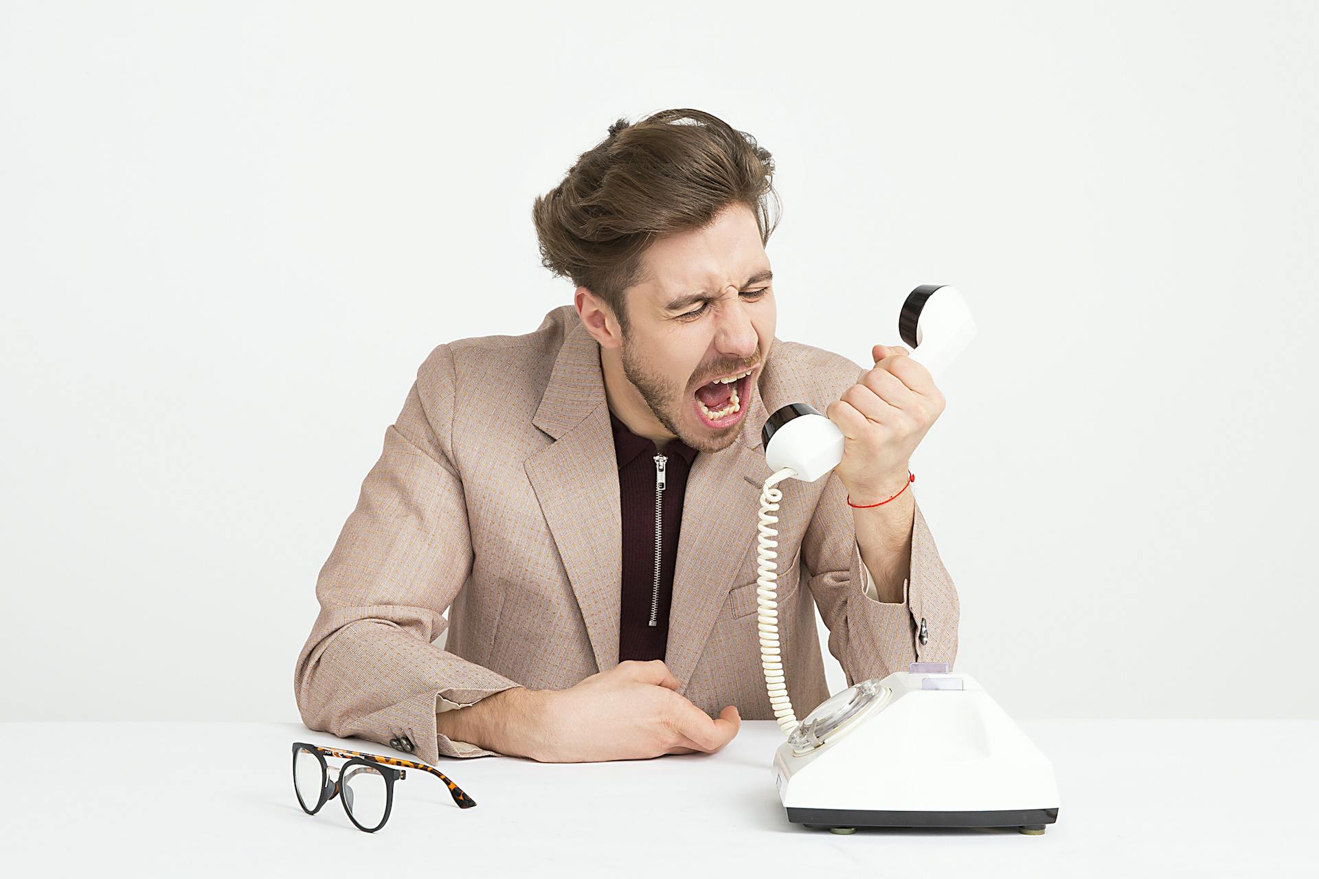 man-wearing-brown-suit-jacket-mocking-on-white-telephone