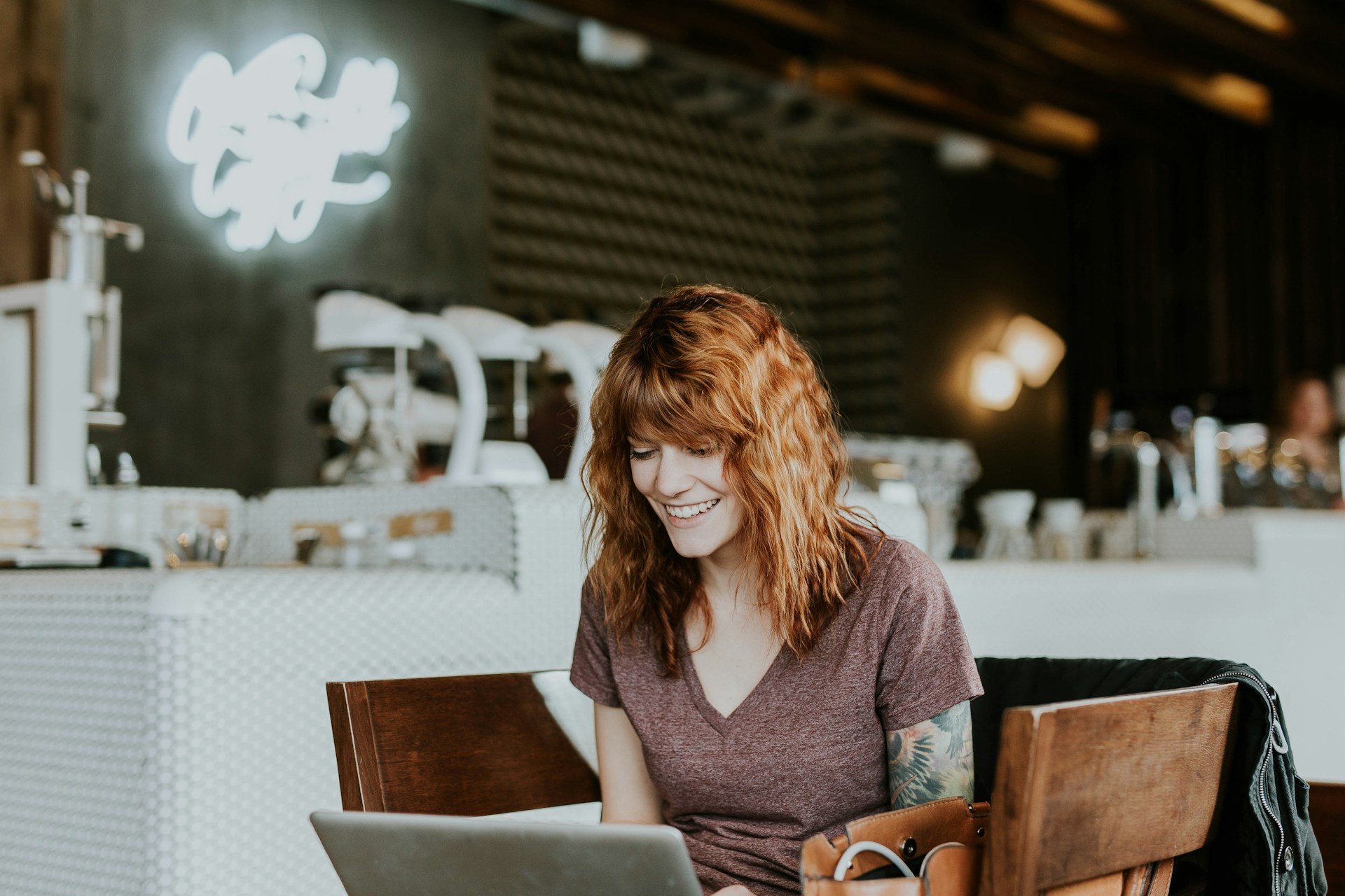 woman-sitting-on-brown-wooden-chair-while-using-silver-laptop