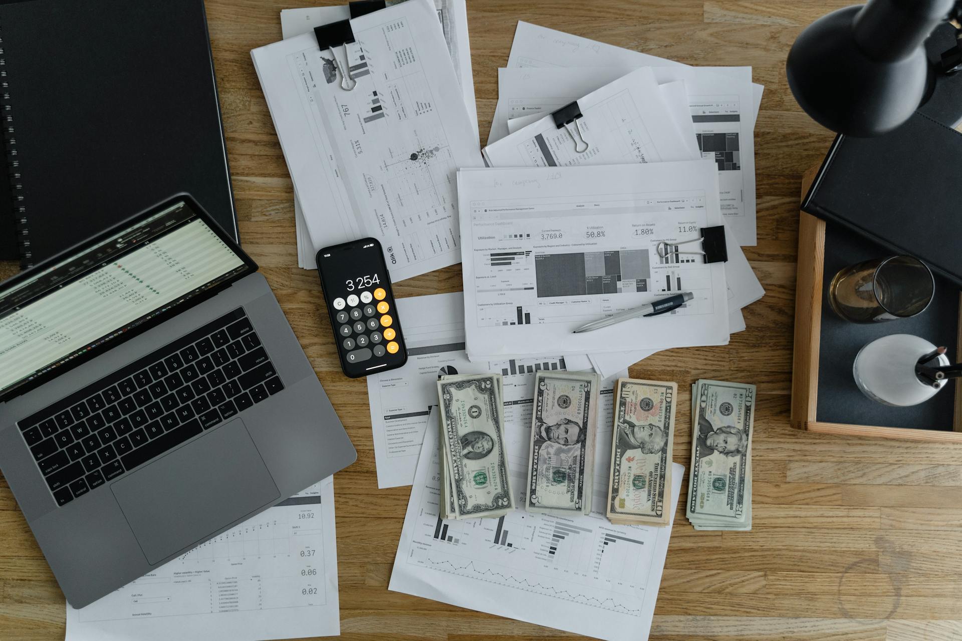 a-laptop-near-the-dollars-and-papers-on-a-wooden-table