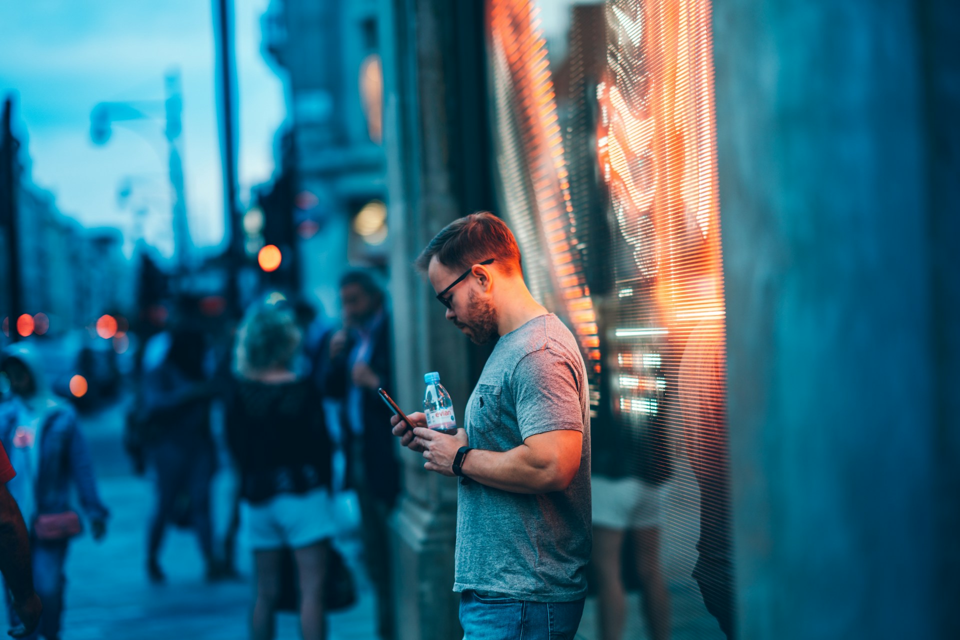 man-standing-beside-wall-holding-smartphone-and-water-bottle
