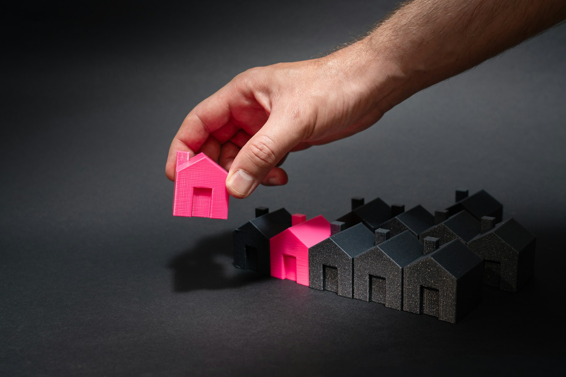a-hand-reaching-for-a-pink-house-in-front-of-a-row-of-houses