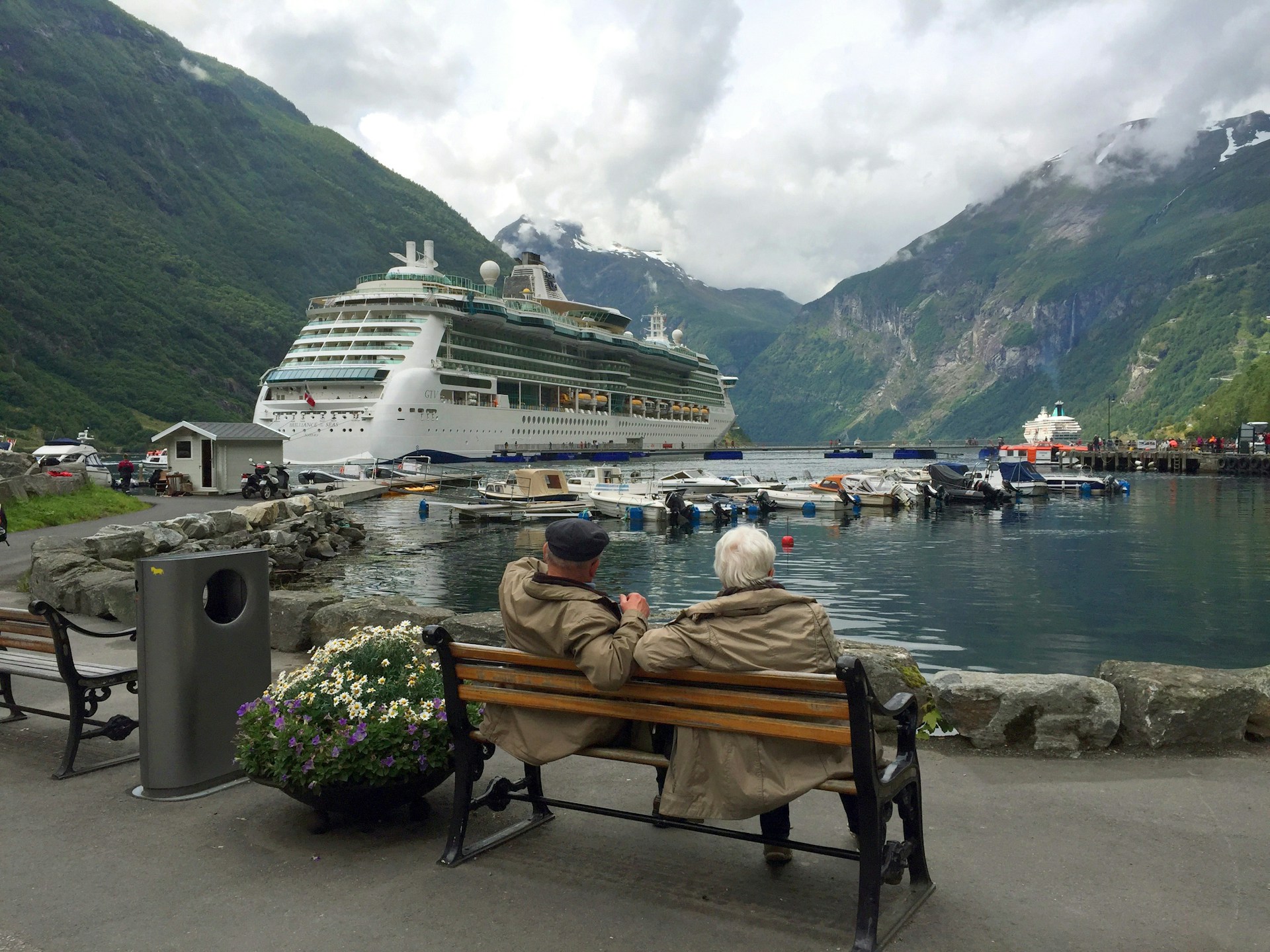 woman-in-brown-coat-sitting-on-brown-wooden-bench-near-white-cruise-ship-during-daytime